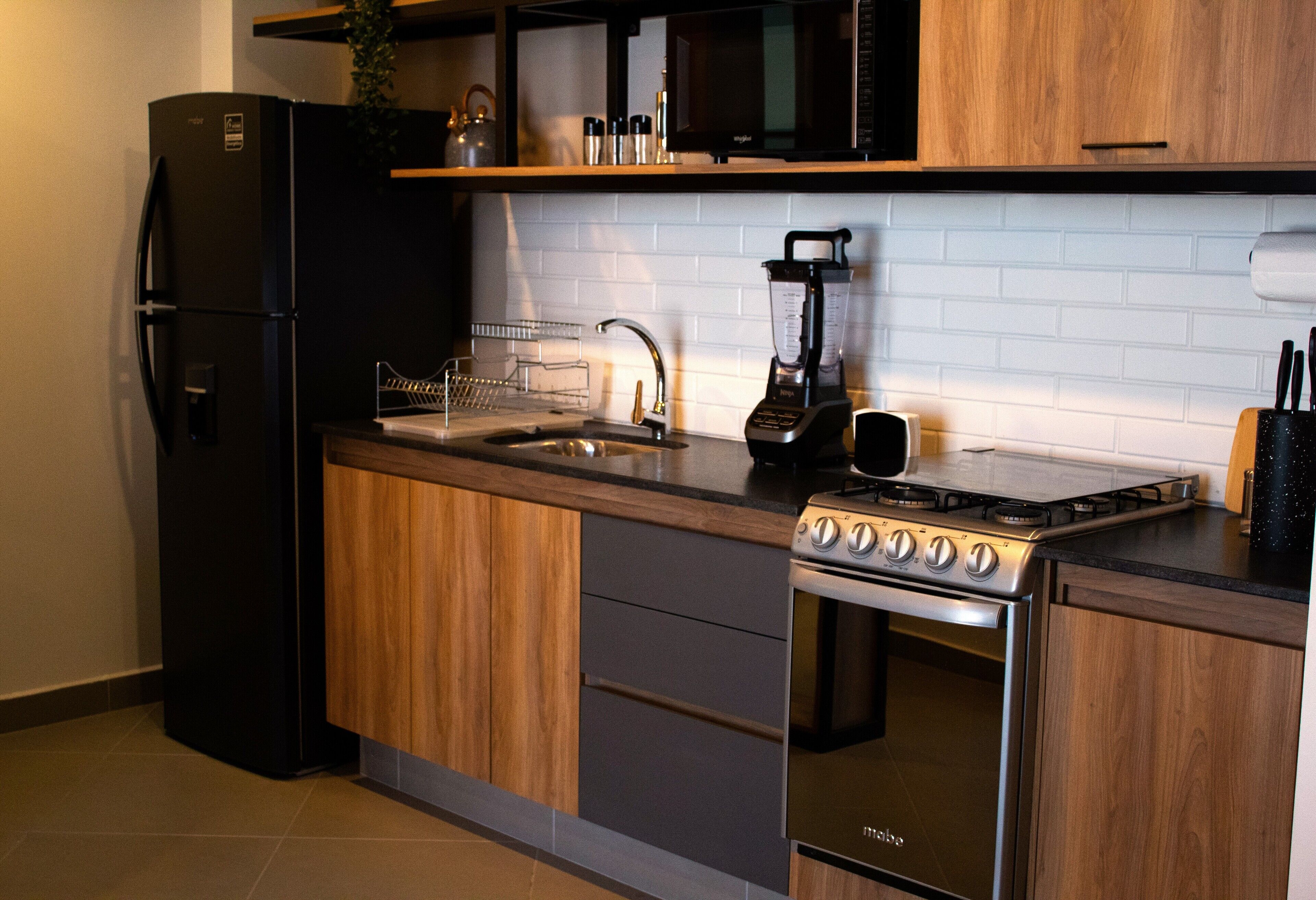 Una cocina moderna con un refrigerador negro, estufa de acero inoxidable y un microondas sobre una encimera de madera.