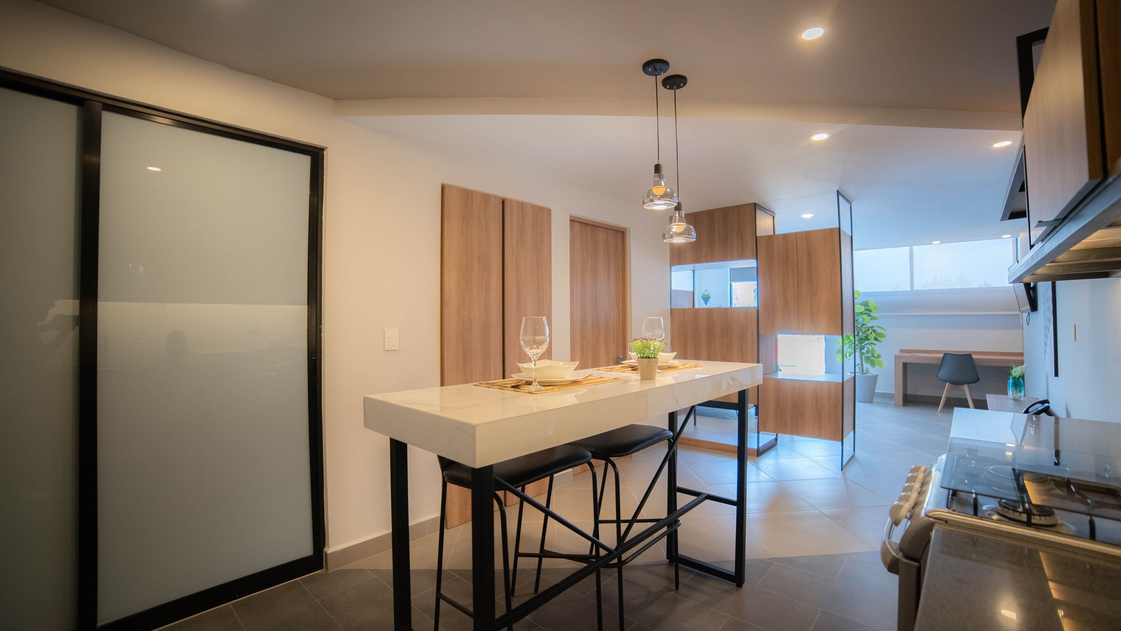 A modern kitchen with a central island, bar stools, pendant lighting, and a view into the dining area.