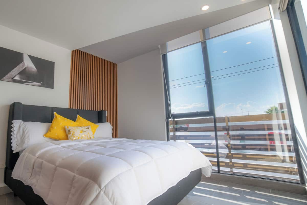 Un dormitorio moderno con una cama grande, vista del cielo a través de una ventana y un panel de pared de madera.