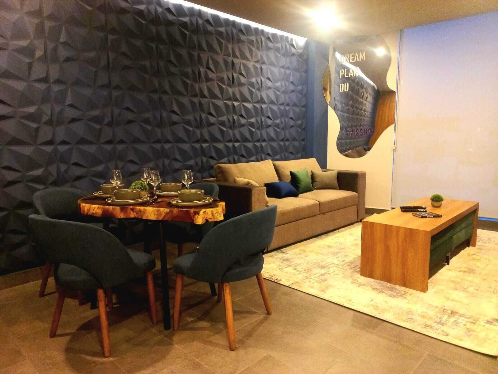 Una sala moderna con pared de diseño geométrico, un sofá, una mesa de comedor con platos y vasos, y una pequeña mesita de madera.