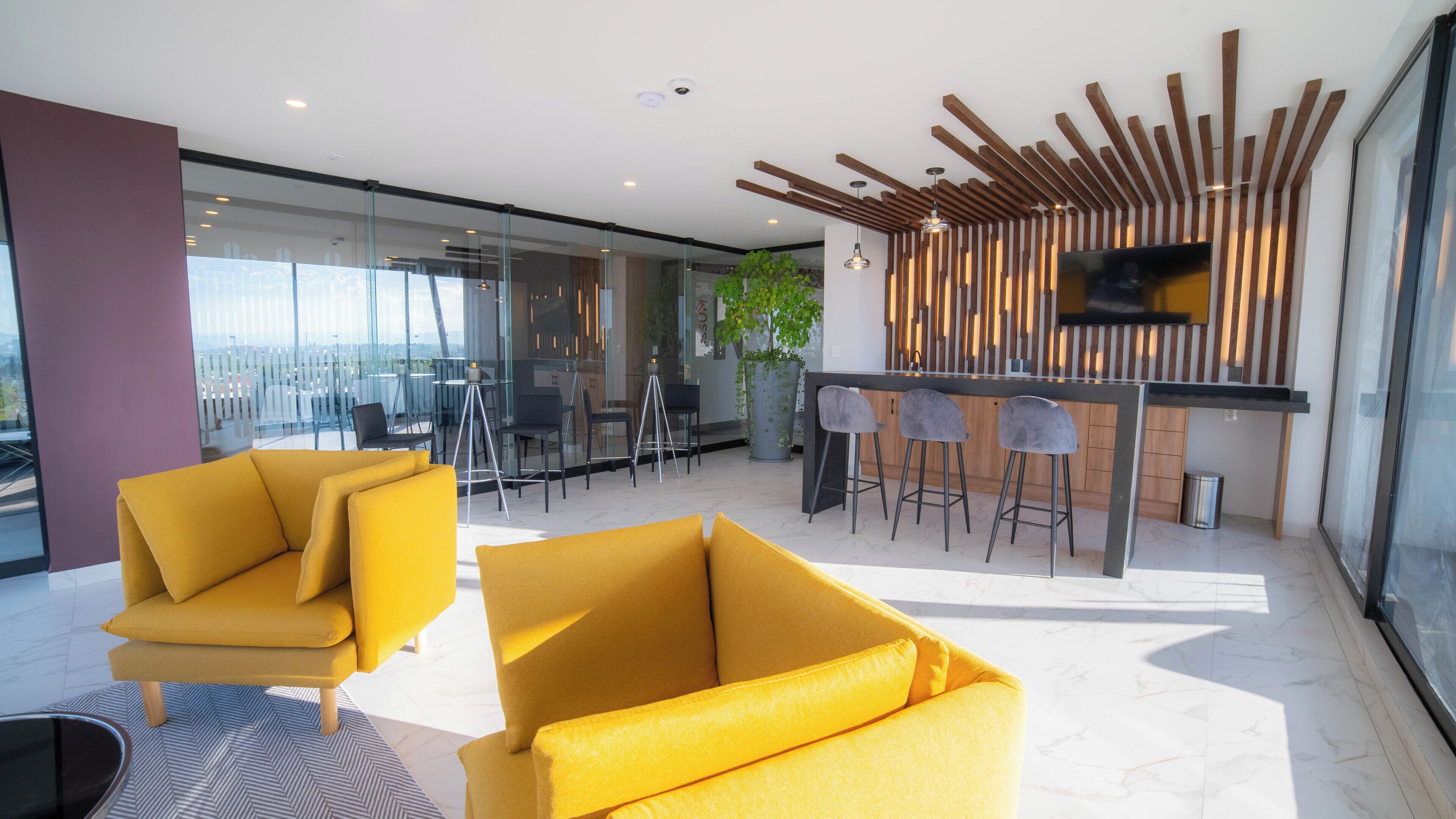 A modern interior with yellow sofas, a bar area, and a large window offering a view.