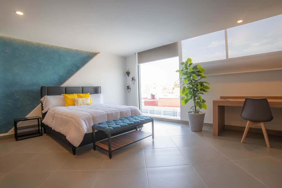 Un dormitorio moderno con cama, banco, escritorio y planta en maceta.
