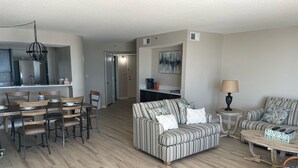 A modern living room with a striped sofa, a dining table with chairs, a coffee table, and a kitchen area with a refrigerator and dining table. -  Sea Castle 5E. Fastidiously Clean  Ocean Front Condo RENOVATED (North Myrtle Beach)
