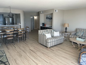 Uma sala de estar moderna com um sofá listrado, uma mesa de jantar com cadeiras, uma mesa de centro e uma área de cozinha com geladeira e mesa de jantar.
