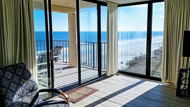 A spacious balcony with a view of the beach, a patterned chair, and a wooden floor. -  Sea Castle 5E. Fastidiously Clean  Ocean Front Condo RENOVATED (North Myrtle Beach)