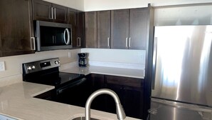 A modern kitchen with dark wooden cabinets, a stainless steel refrigerator, a microwave, and a black stove. -  Sea Castle 5E. Fastidiously Clean  Ocean Front Condo RENOVATED (North Myrtle Beach)
