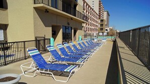 A row of blue lounge chairs on a concrete deck with a metal railing, a building with balconies, and a clear sky. -  Sea Castle 5E. Fastidiously Clean  Ocean Front Condo RENOVATED (North Myrtle Beach)