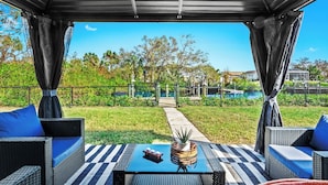 Eine Terrasse im Freien mit Korbmöbeln, einem Tisch mit Kerzen und Blick auf einen Pool und Grünflächen.