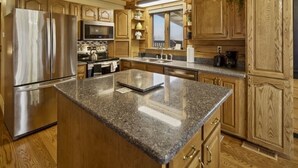 Eine Küche mit Holzausstattung, einem Edelstahlkühlschrank, Granitarbeitsplatten und einem eingebauten Backofen.