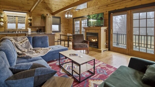 Ein gemütliches Blockhauss-Interieur mit Wohnbereich, Kamin, Fernseher und Küchenzeile.