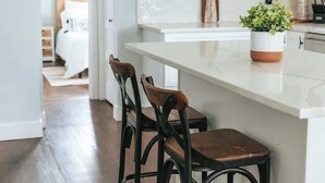 Uma cozinha com armários brancos, uma ilha de madeira com banquetas e um pendente.