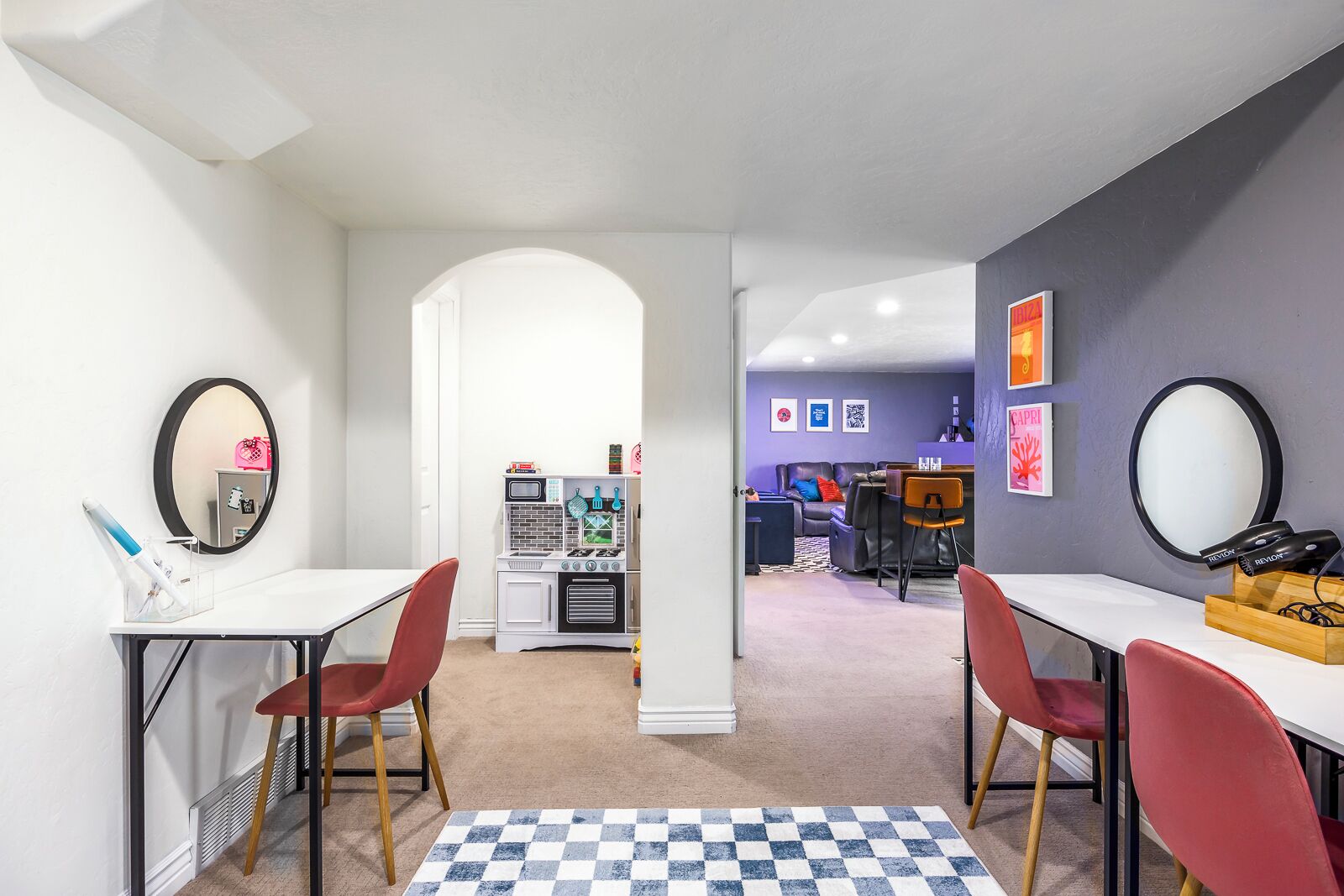 Una habitación de hotel moderna con kitchenette, un área de comedor con sillas rojas y una alfombra de cuadros.