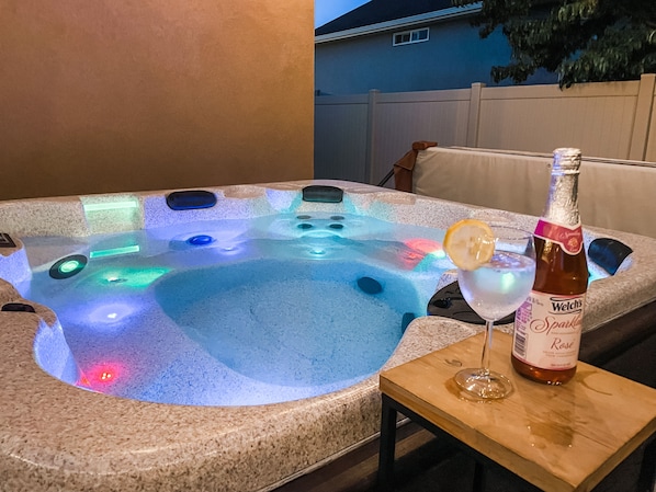 Un jacuzzi con luces LED de colores, una botella de vino Welch's Sparkling Rosé y una copa de cóctel con una rodaja de limón sobre una mesa de madera.