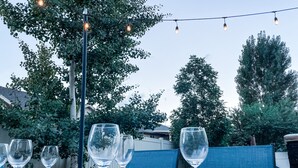 Een buitenterras met tafels voor twee personen, omringd door bomen en een blauwe hek.