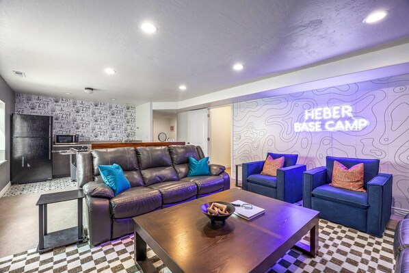 A modern living room with a leather sofa, two blue armchairs, a wooden coffee table, and a kitchen area with a microwave and refrigerator. - Summer Promotion- XBOX room- Pets welcomed! Sleeps 18- Hottub- Hammocks (Heber City)