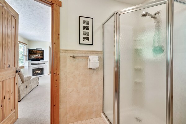 Un baño con cabina de ducha de vidrio, una toalla blanca colgada en un perchero y una foto en un marco en la pared.