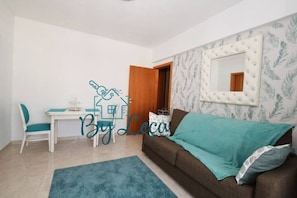 A living room with a sofa, a table with chairs, a mirror, and a door leading to another room.