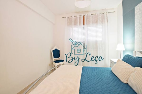 A bedroom with a bed, a chair, a nightstand, and a window with curtains.