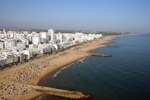 A coastal cityscape with a long sandy beach, high-rise buildings, and a clear sky.