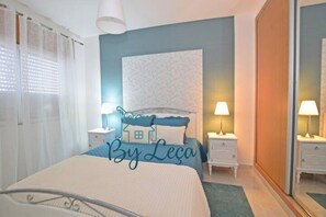 Un dormitorio con cama, mesitas de noche, lámpara, ventana con cortinas y pared con textura.