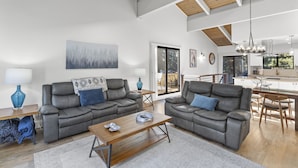 A spacious living room with two grey leather sofas, a wooden coffee table, and a painting on the wall. A dining area with a wooden table and chairs is visible in the background. - Newly Rennovated and Air Conditioned Townhouse -1 mile from Skiing (Incline Village)