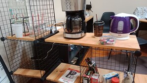 Un petit coin cuisine équipé d’une machine à café, d’une tasse, d’une bouilloire et de divers produits alimentaires.