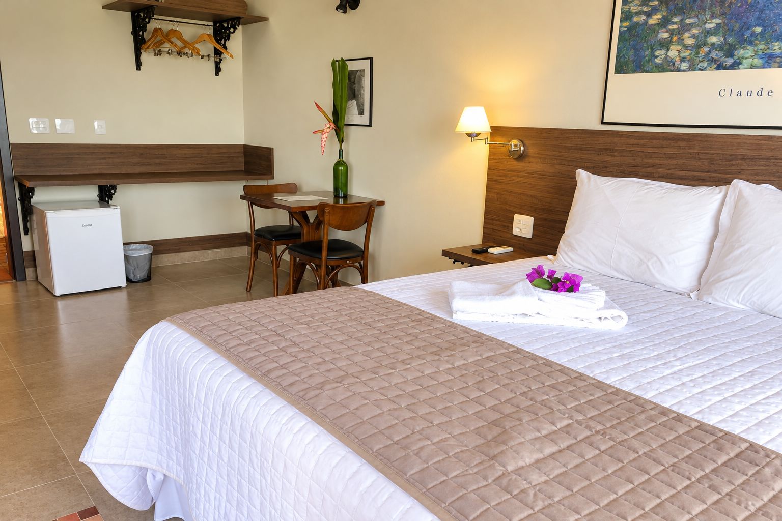 Una camera d'albergo con un letto, una scrivania, una sedia, un comodino, una lampada e un quadro appeso al muro.