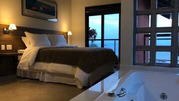 Ein Schlafzimmer mit einem großen Bett, einer Badewanne und Meerblick durch ein großes Fenster.