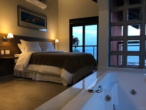 A bedroom with a large bed, a bathtub, and a view of the sea through a large window. - Refúgio do Cacupé (Florianópolis)