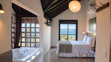 Un dormitorio con una ventana grande, una cama, una bañera y vistas al mar.