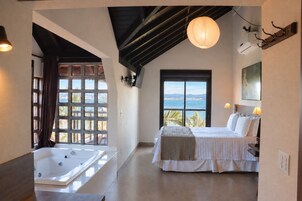 Un dormitorio con una ventana grande, una cama, una bañera y vistas al mar.