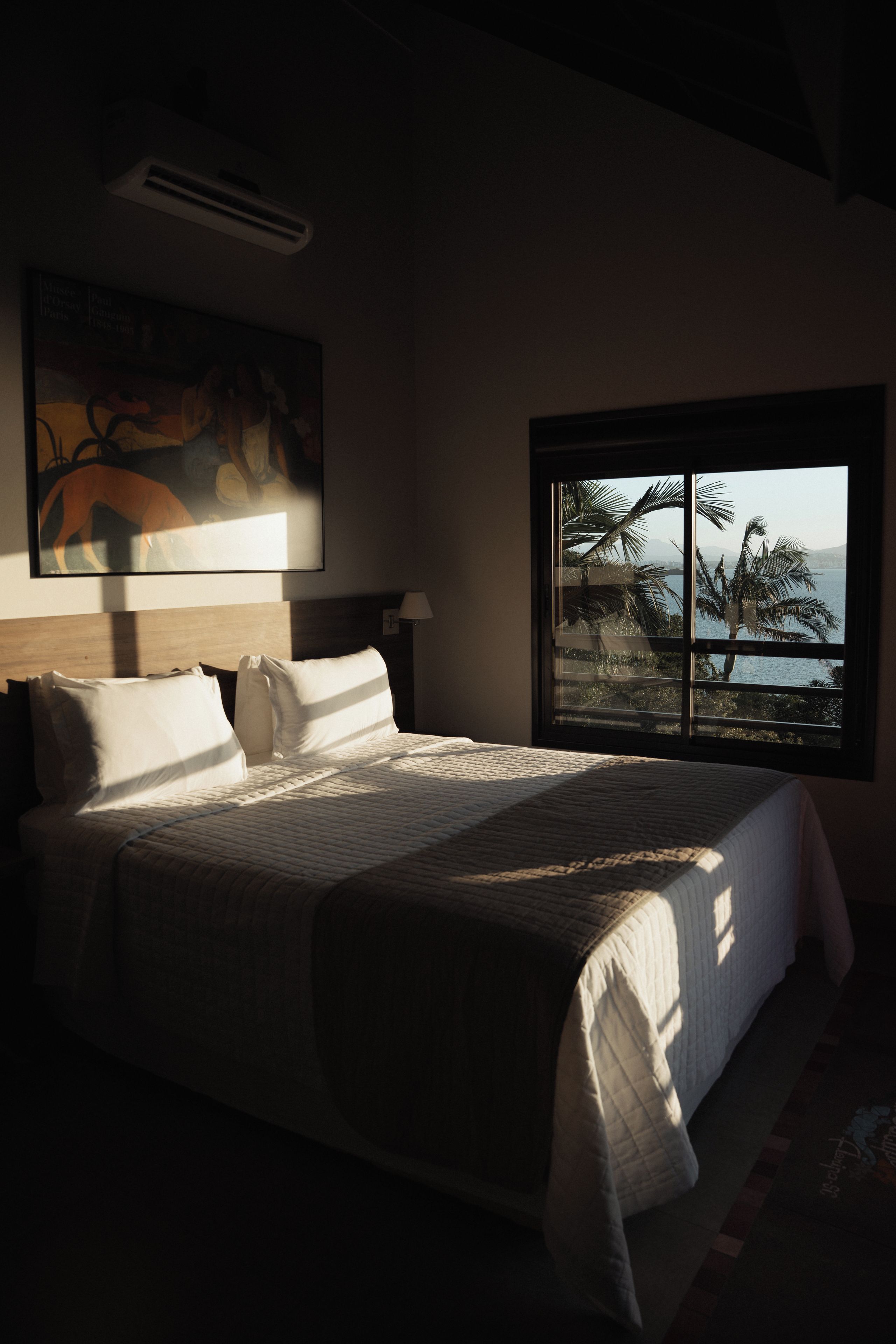 Ein Bett mit Blick auf eine Palme und Wasser durch ein Fenster.