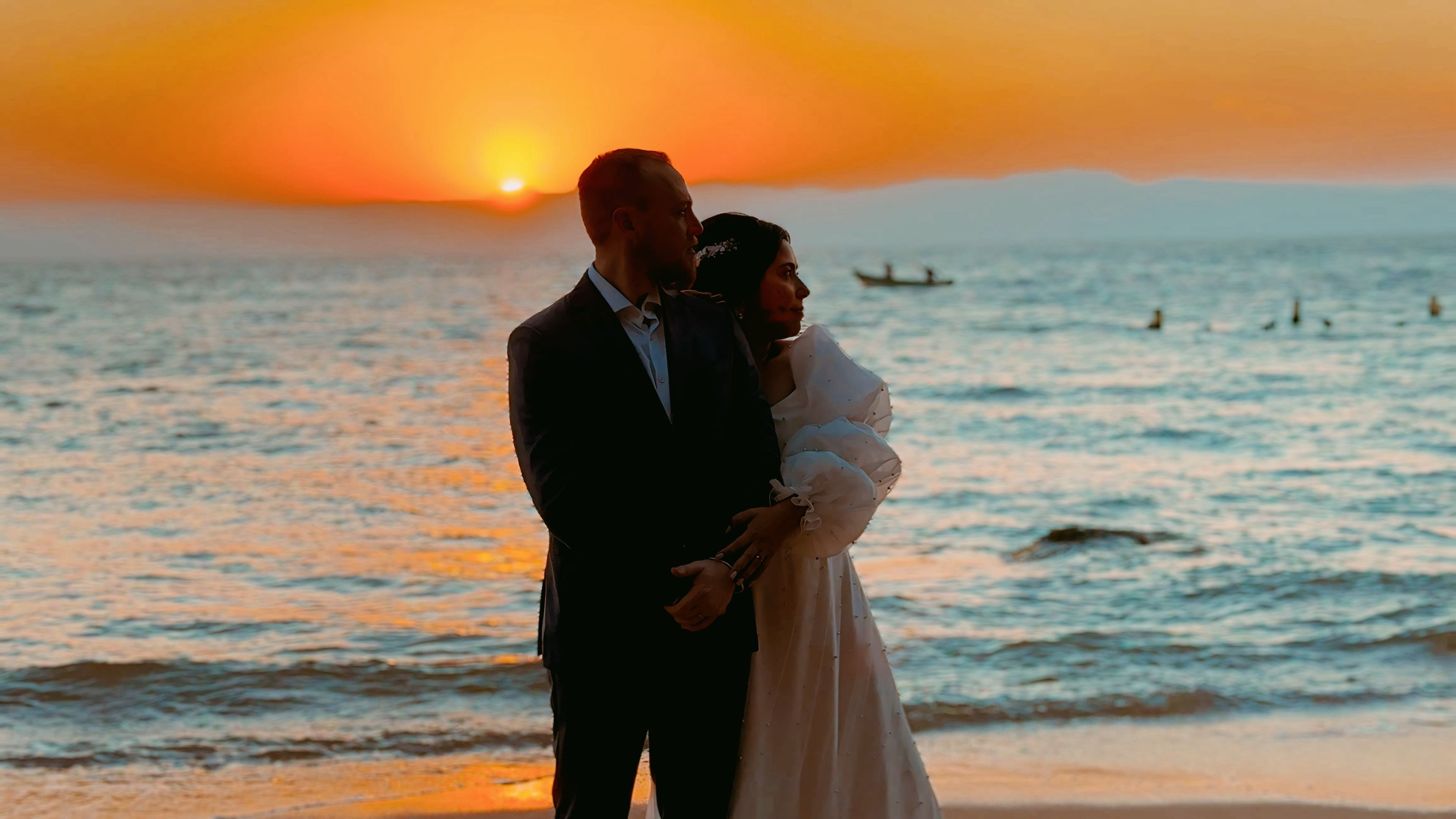 Una pareja se abraza en una playa al atardecer, con el océano de fondo.
