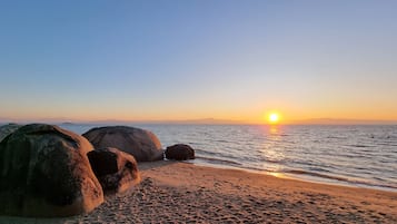Una platja amb roques grans, aigua tranquil·la i un capvespre.