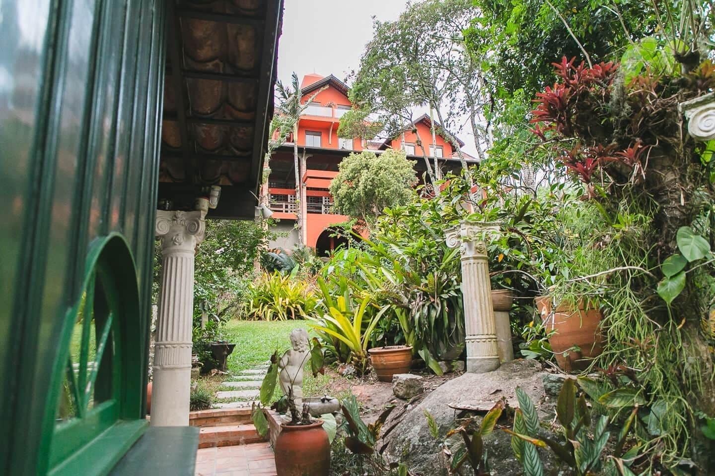 Un giardino rigoglioso con piante in vaso e un vialetto in pietra che conduce a un edificio con tetto rosso.