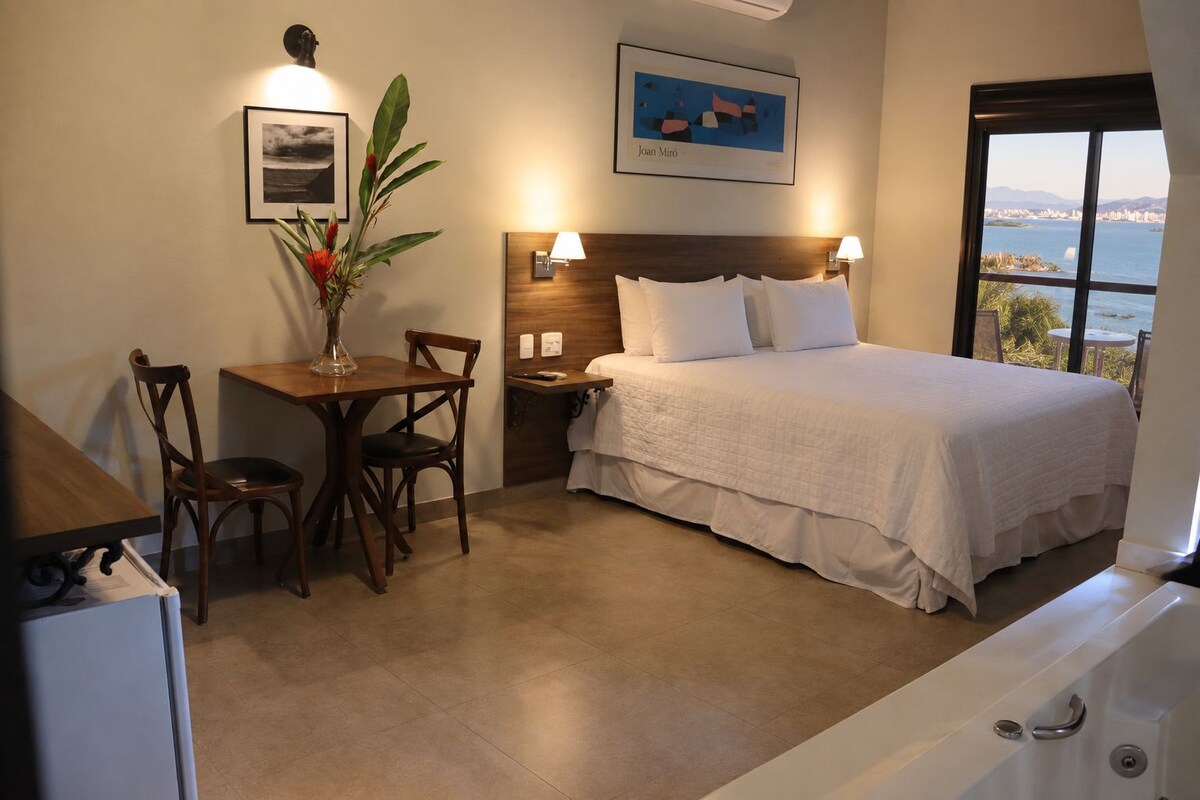 Una camera d'albergo con un letto, una scrivania con una sedia, un vaso con fiori e un quadro appeso al muro.