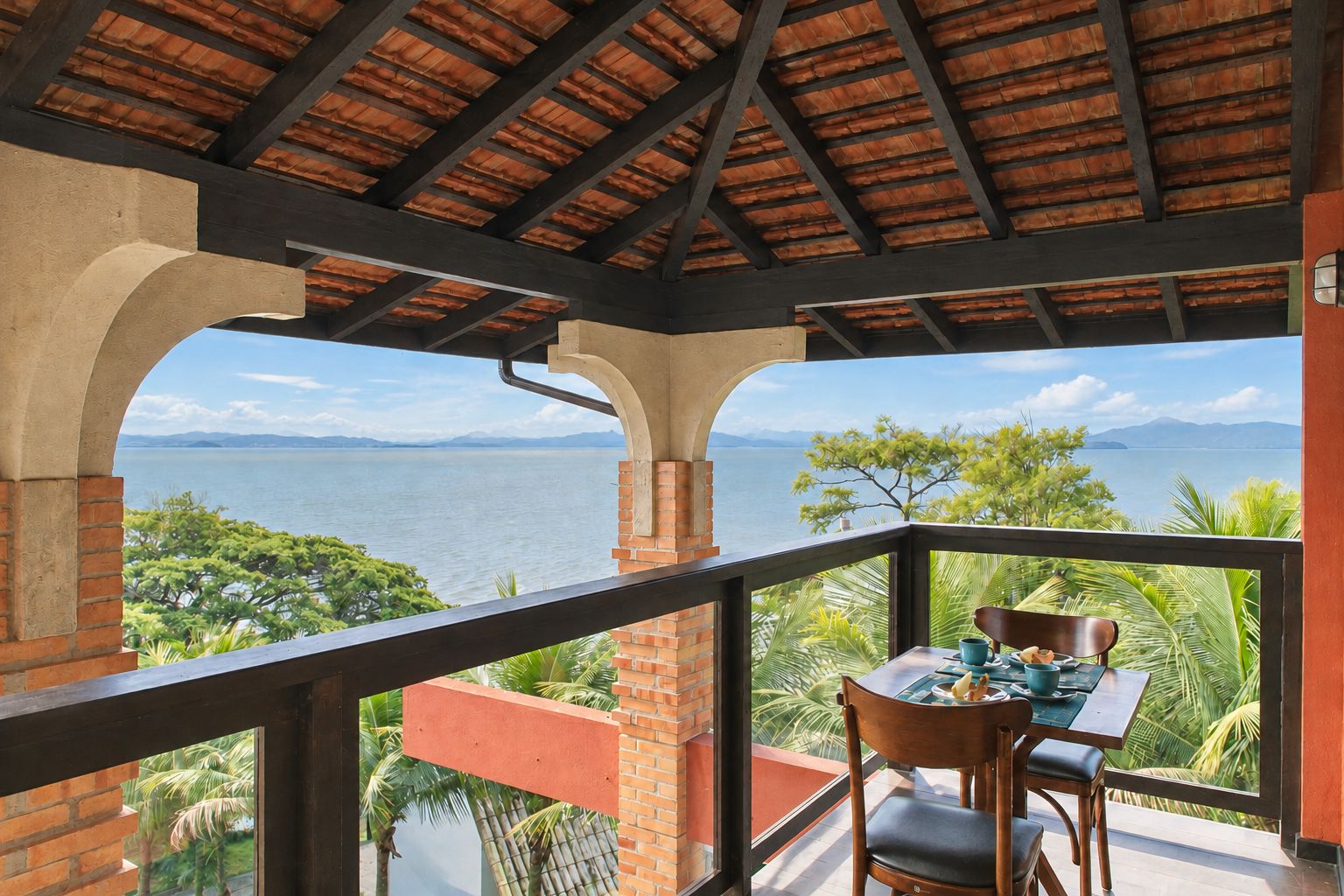 A balcony with a table and chairs overlooking a body of water and mountains.