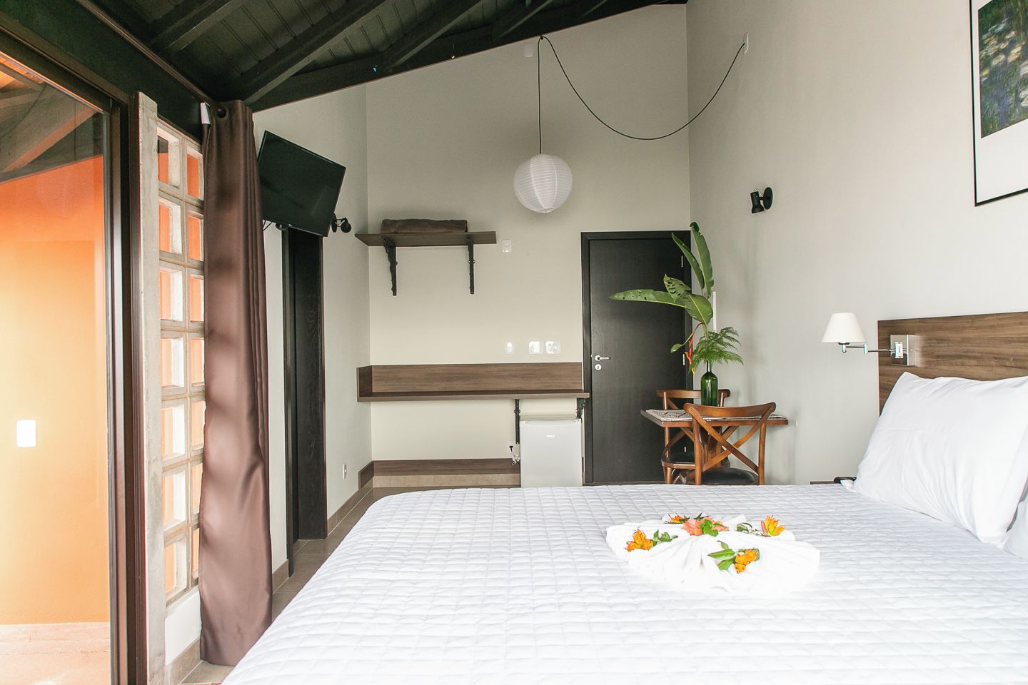 Una camera d'albergo con un letto, una scrivania, una sedia, una pianta e una porta.