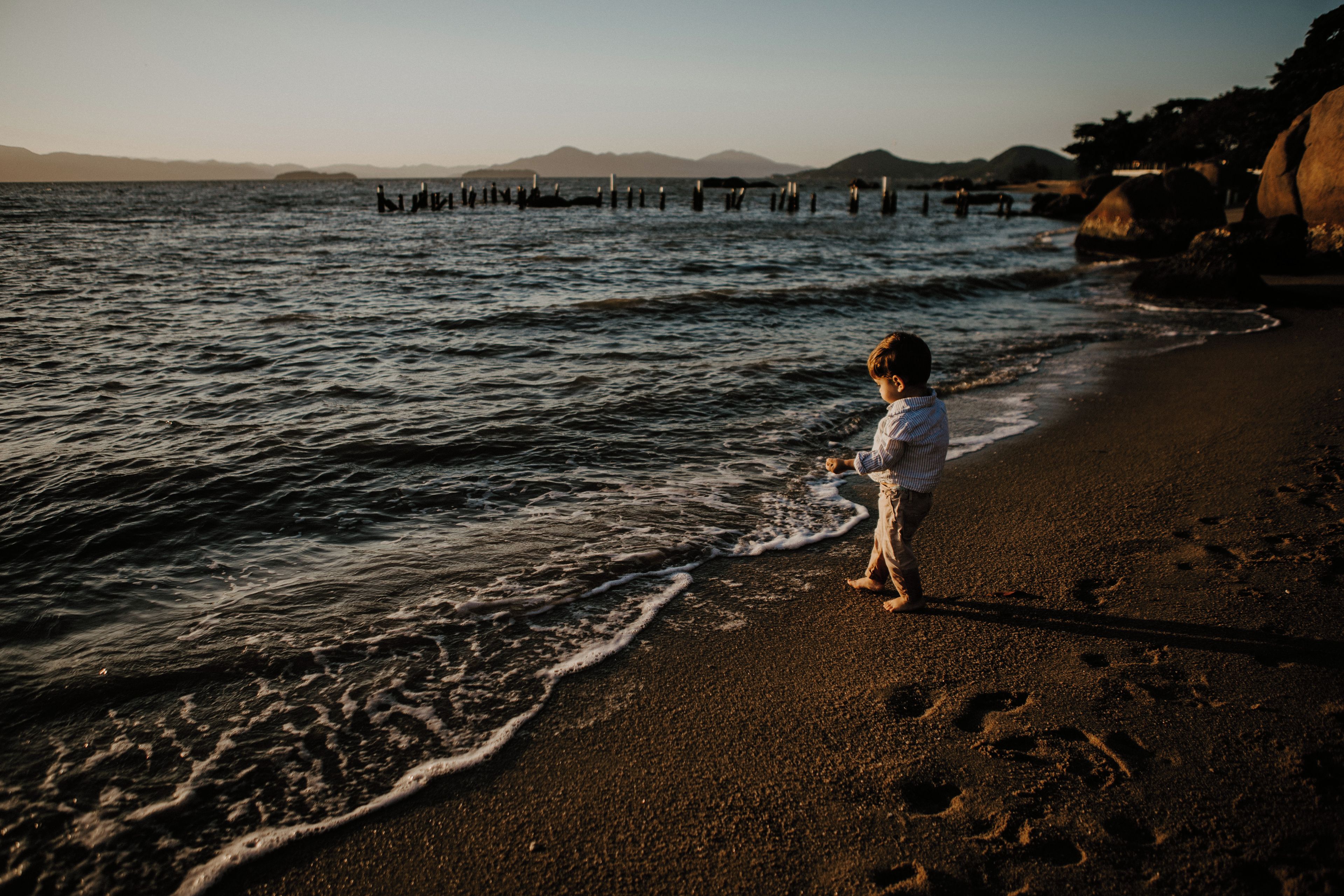 Un niño de pie en una playa arenosa, con el océano al fondo.
