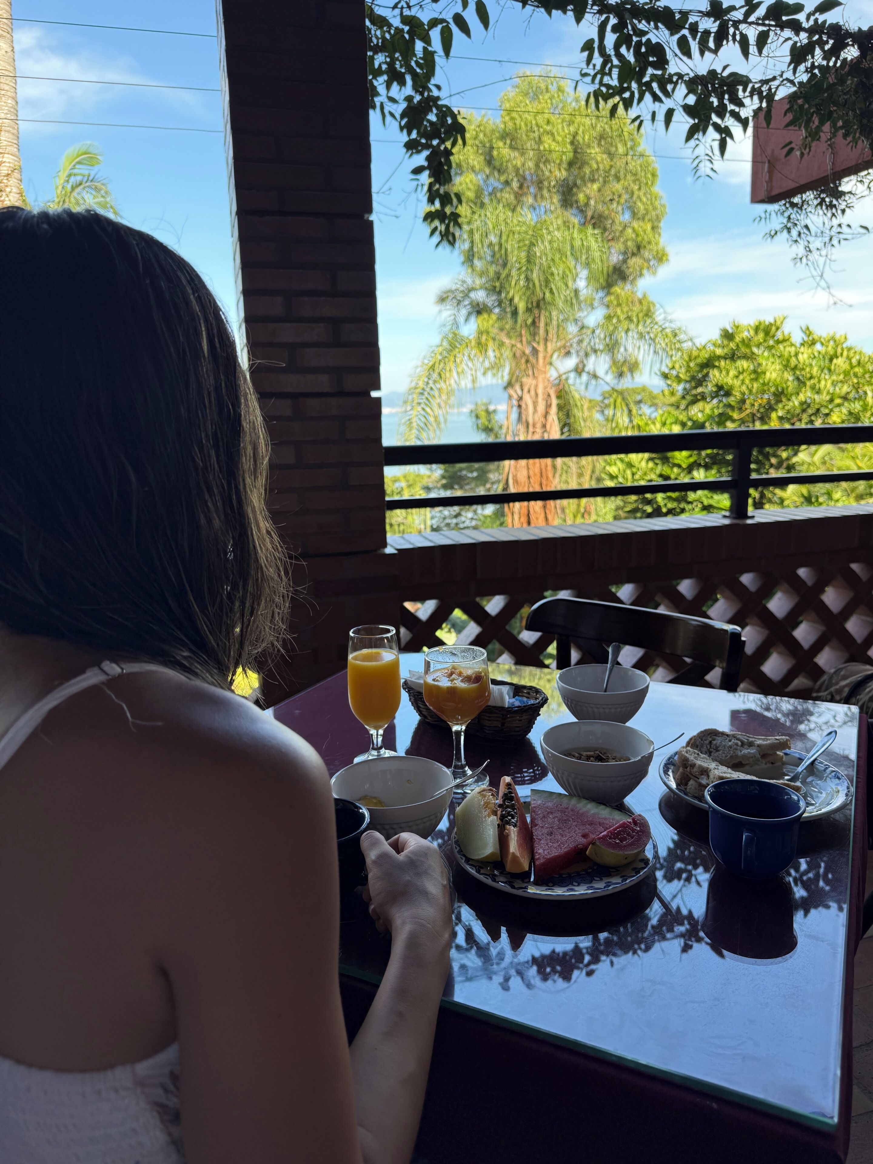 Eine Person sitzt an einem Tisch mit Blick auf Bäume und einen klaren Himmel.