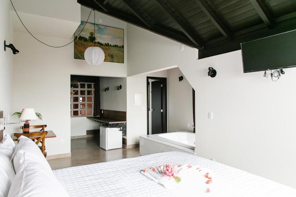A modern bedroom with a large bed, a small kitchenette, and a bathroom with a bathtub.