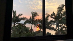 A sunset view through a window with palm trees and a clear sky. - Refúgio do Cacupé (Florianópolis)