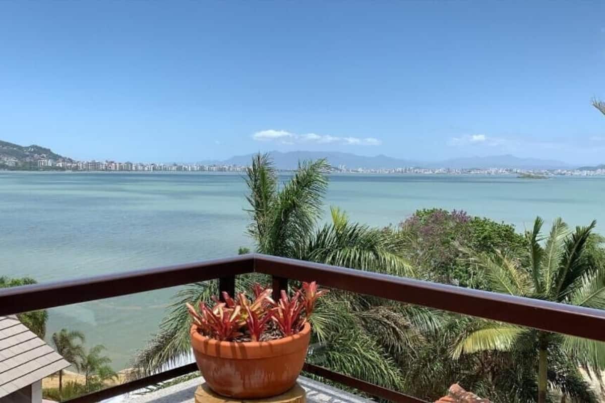 Varanda com vista para um mar tranquilo e montanhas ao longe.
