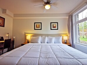 Une chambre d’hôtel avec un grand lit, deux lampes de chevet, un ventilateur de plafond et des œuvres d’art encadrées accrochées au mur.