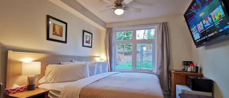 A hotel room with a bed, bedside tables, a TV, and a window with a view of greenery.