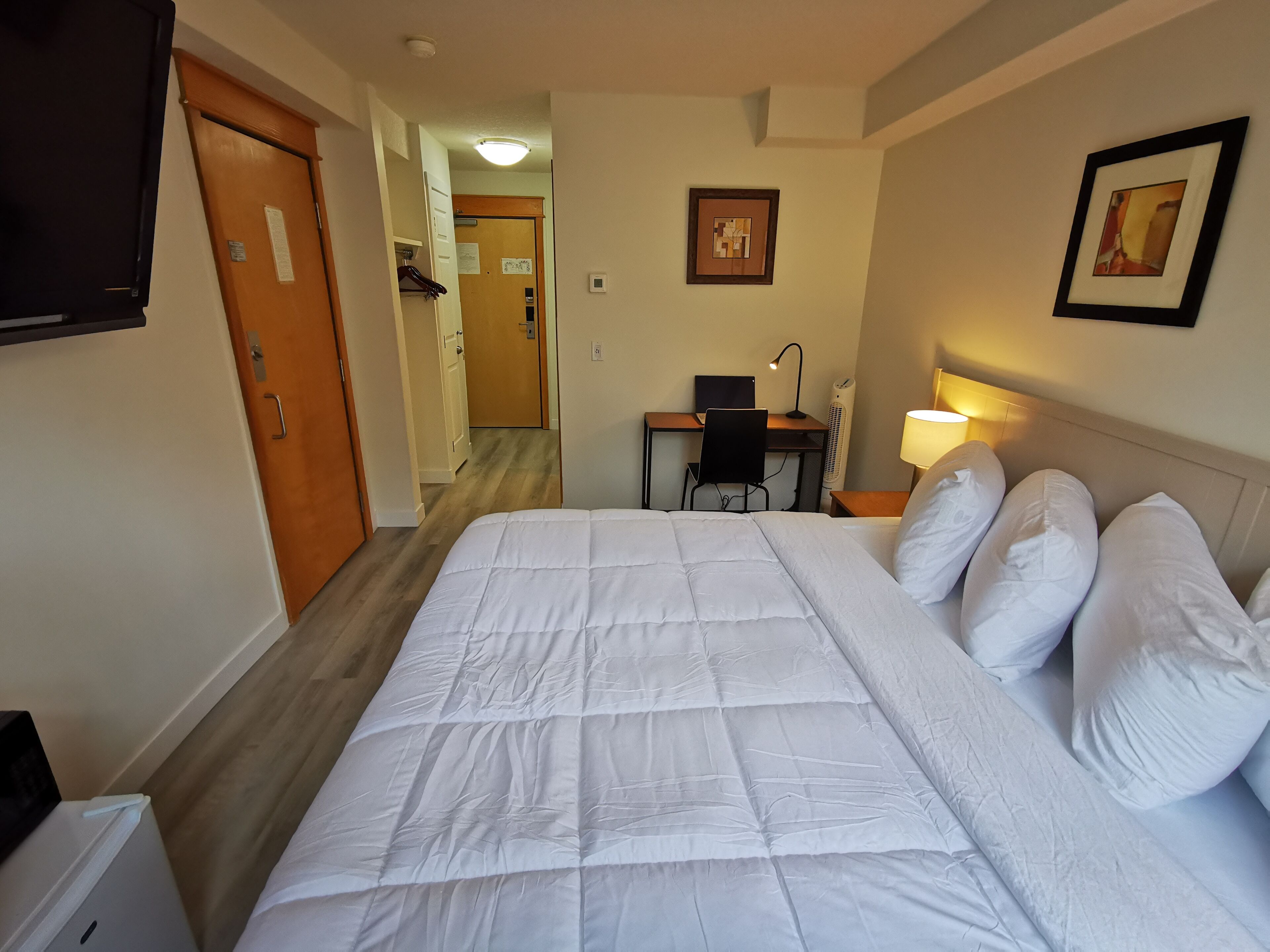 Habitación de hotel con una cama grande, un escritorio con silla, una lámpara de escritorio y un televisor montado en la pared.