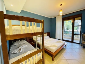 A room with two beds, one with a wooden headboard and the other with a plain headboard. There is a window with a view of the outside.