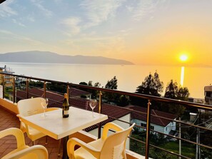 Ein Balkon mit Tisch und Stühlen mit Blick auf einen See bei Sonnenuntergang.