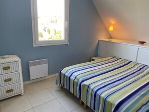 Une chambre à coucher comprenant un lit, une commode, un radiateur, une fenêtre et une lampe fixée au mur.