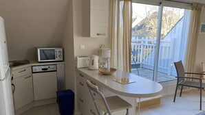 Una cocina compacta equipada con microondas, tostadora y hervidor, un pequeño comedor con mesa y sillas, y vista a un espacio exterior cercado.